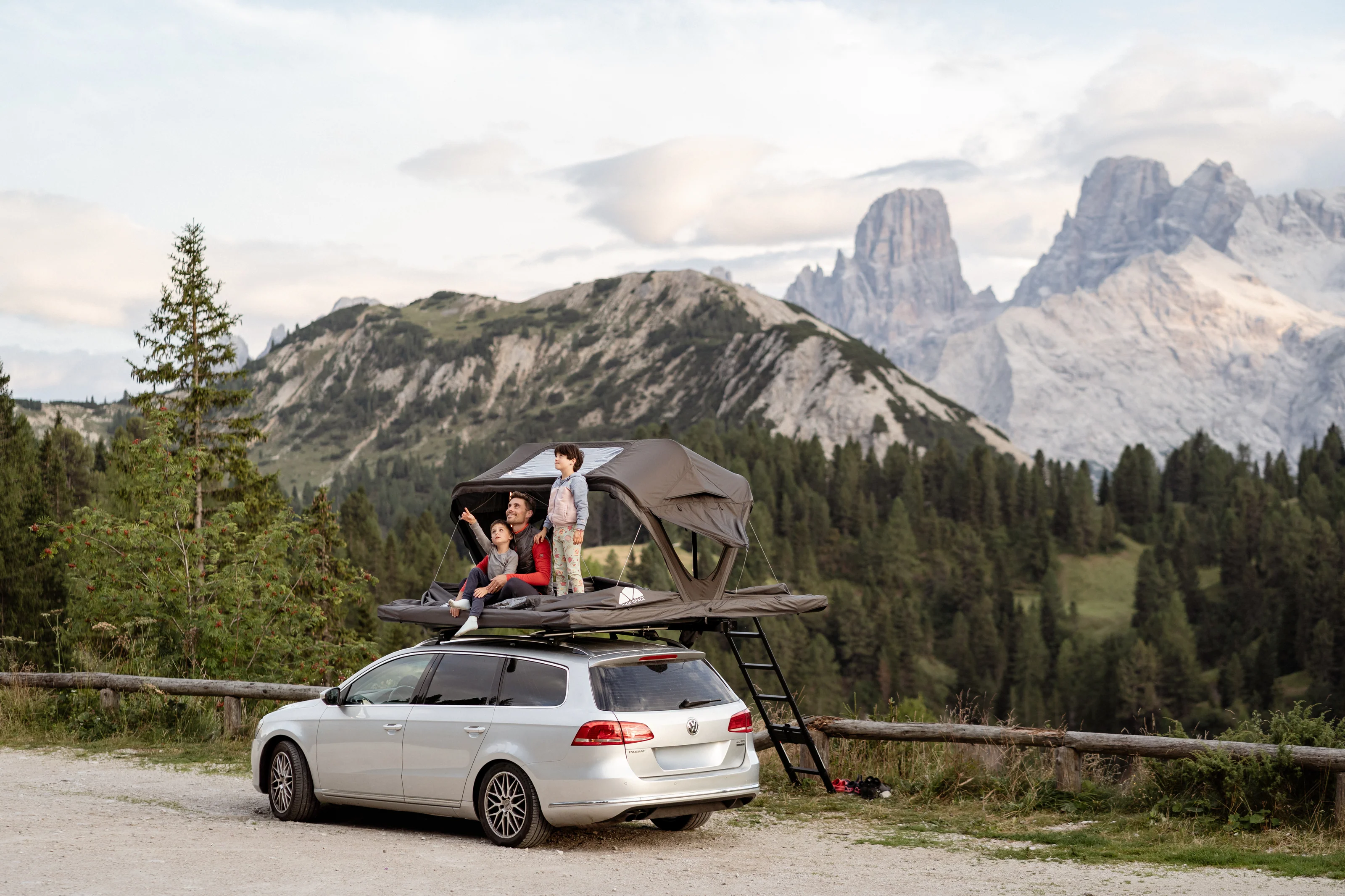 Famille installée dans une tente de toit souple sur voiture en montagne, vue sur les Dolomites