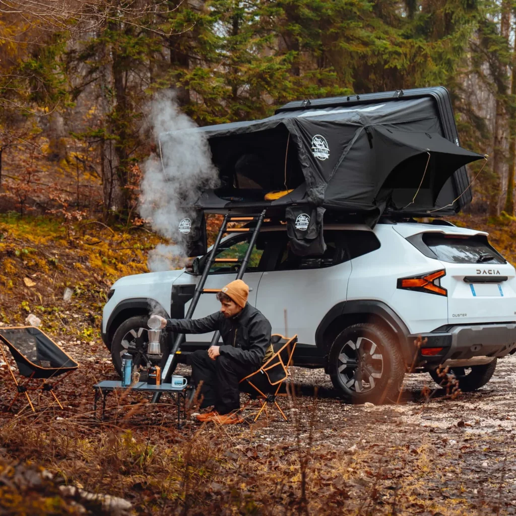 Homme seul installant une tente de toit sur un Dacia Duster en forêt, campant en pleine nature