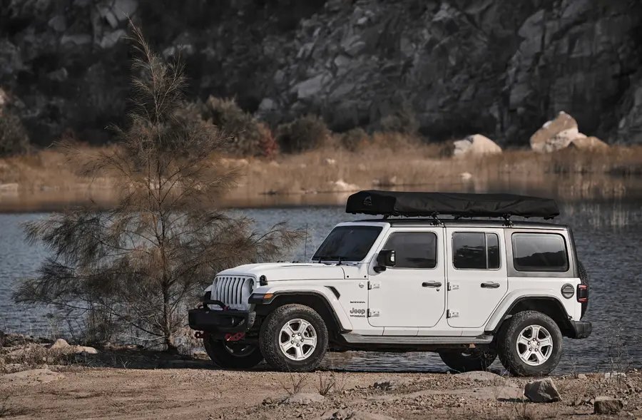 Jeep Wrangler blanc équipé d'une tente de toit souple, garé au bord d'un lac en pleine nature