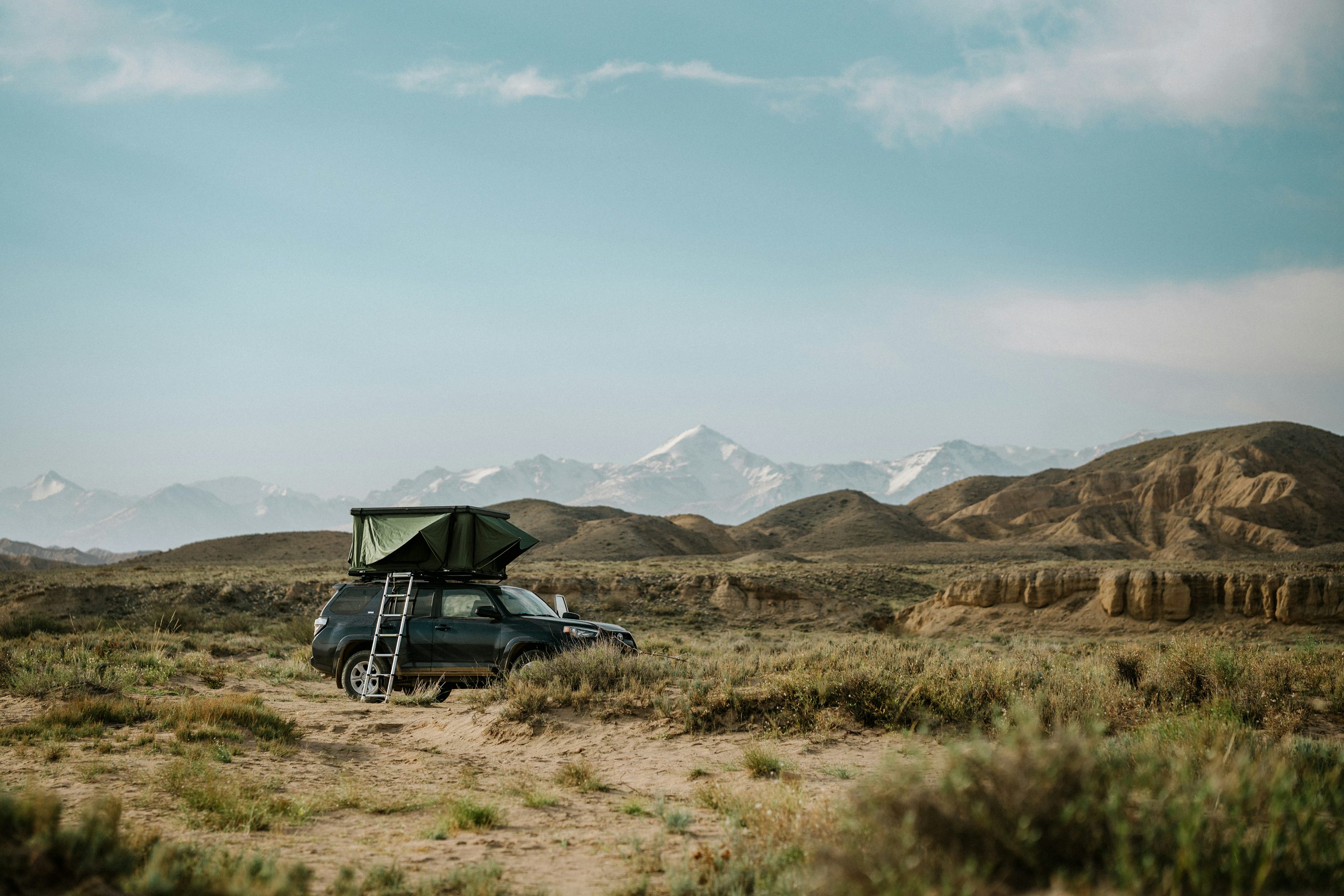 Tente de toit rigide verte ouverte sur un 4x4 noir en pleine nature désertique avec montagnes enneigées